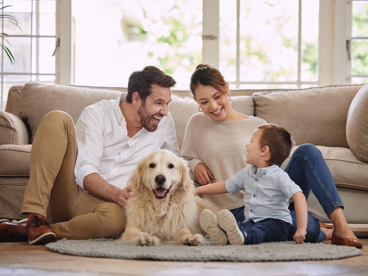 A family relaxing on the living room floor with their golden retriever